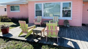 Ein rosafarbenes Haus mit einer Holzterrasse, zwei Adirondack-Stühlen und einem kleinen Tisch.