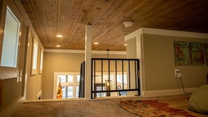 Una habitación espaciosa con un alto techo de madera, un ventanal y vistas a un balcón.