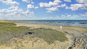 Una playa con arena, dunas cubiertas de hierba y el océano.