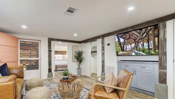 Una sala de estar moderna con sofá, reposapiés y sillón, televisor y un amplio ventanal con vista a la playa.
