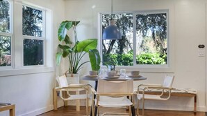 A dining area with a round table, four chairs, a potted plant, and a hanging light fixture. - Zen Garden Retreat | near UO | Fast WiFi | Views (Eugene)