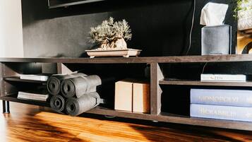 A wooden TV stand with a potted plant, rolled-up mats, and board games.