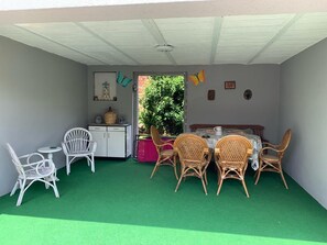 A covered patio area with a green artificial turf floor, white wicker furniture, and a table with a white tablecloth. - House MayFa (Riedseltz)