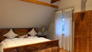 Une chambre à coucher avec un lit en bois, une table de chevet, une armoire et une fenêtre avec des rideaux.