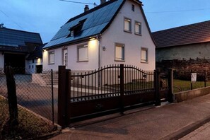 A two-story house with a dark roof, a gated entrance, and a small front yard. - House MayFa (Riedseltz)