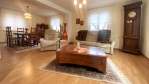 Un salon spacieux avec une table basse en bois, un canapé, une table à manger avec des chaises, un lustre et une horloge.
