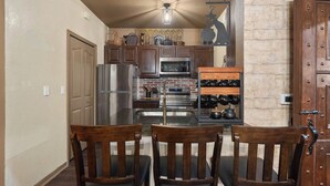 A kitchen with wooden cabinets, a stainless steel refrigerator, a microwave, and a wine rack. - Harry's Hangout at Legacy Dunes | Sage Vacations (Kissimmee)