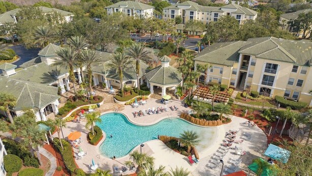 A resort with a central swimming pool, multiple buildings, and palm trees. - Harry's Hangout at Legacy Dunes | Sage Vacations (Kissimmee)