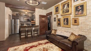 A living room with a brown leather sofa, a red and beige patterned rug, a chandelier, and a kitchen in the background. - Harry's Hangout at Legacy Dunes | Sage Vacations (Kissimmee)