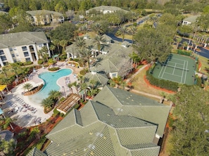Vista aerea di un resort con piscina, campi da tennis e diversi edifici con tetti verdi.
