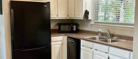 A kitchen with white cabinets, a black refrigerator, a microwave, a dishwasher, and a window with blinds.