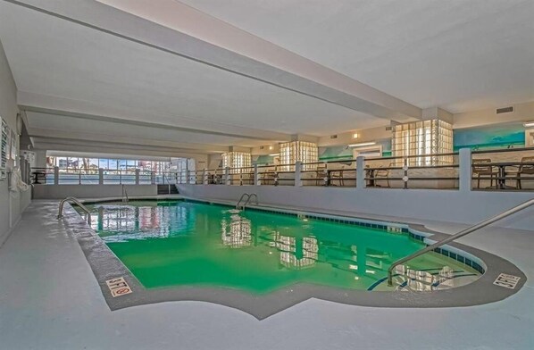 Una piscina interior con agua cristalina, rodeada por una solarium y un muro de vidrio.