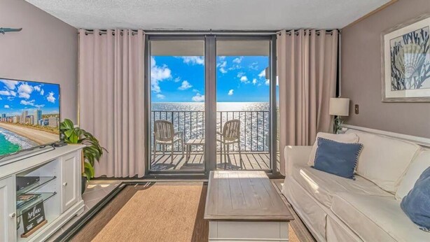 Ein Wohnzimmer mit einem Balkon mit Blick auf einen Strand.
