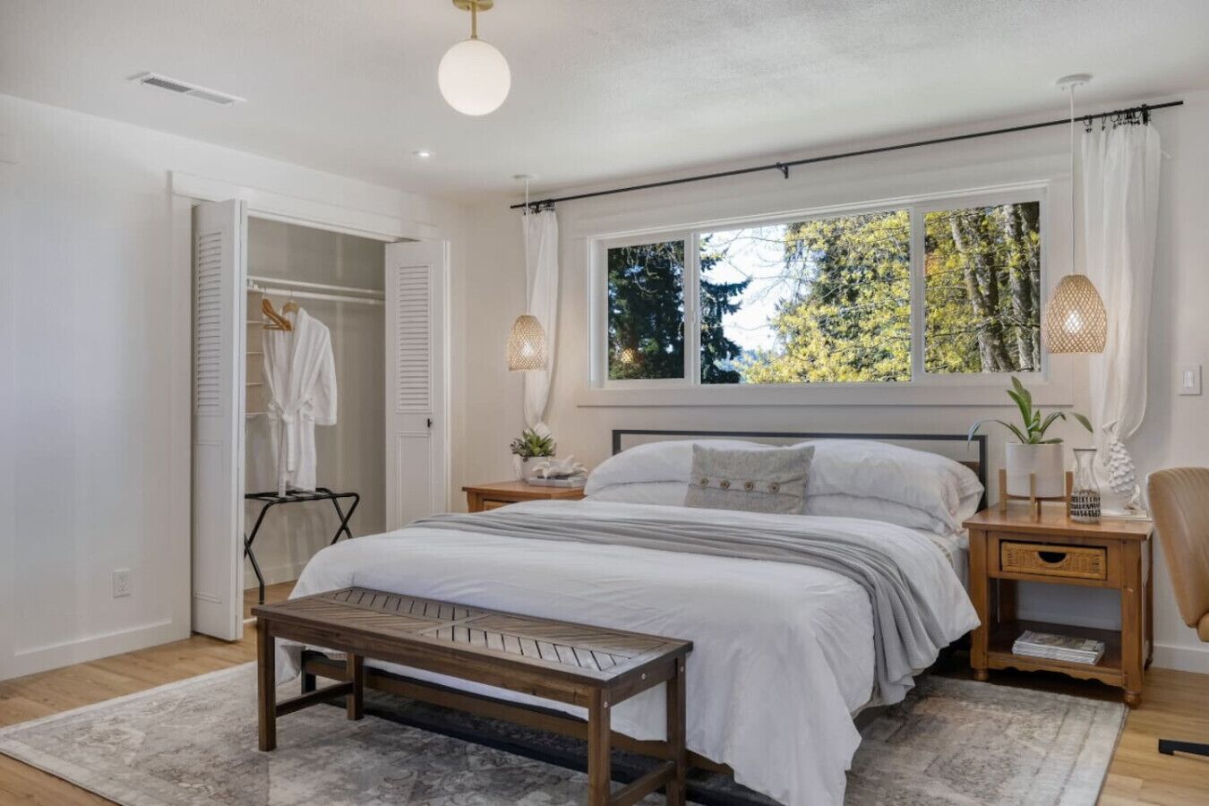 Un dormitorio con cama, mesitas de noche, un banco, una ventana con cortinas y un armario.