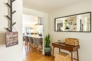 Un espace repas moderne avec une table et des chaises en bois, une enseigne suspendue, un miroir et une plante en pot.