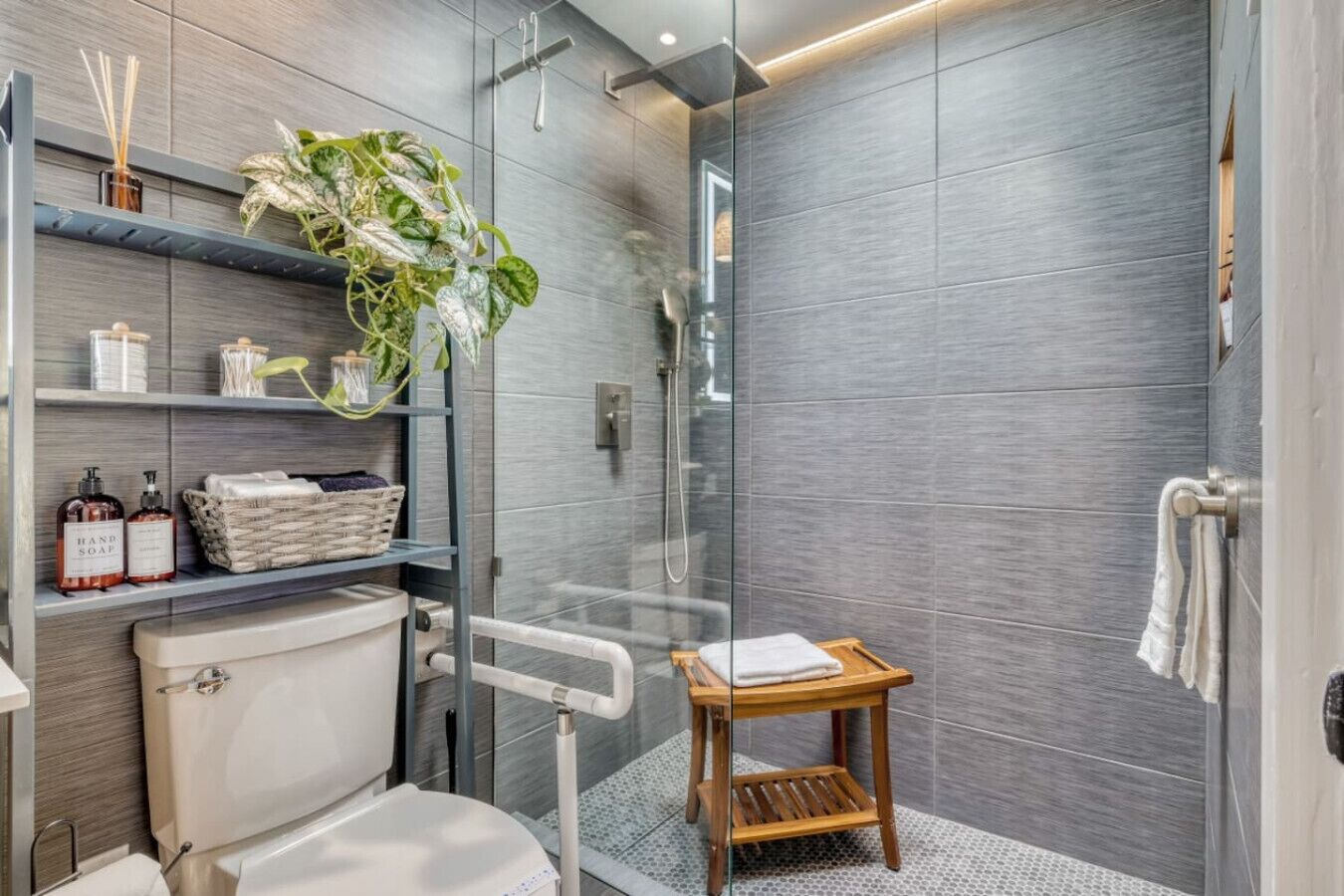 Un baño moderno con cabina de ducha de vidrio, inodoro, lavamanos y un taburete de madera pequeño.