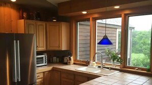 Une cuisine avec des meubles en bois, un réfrigérateur en acier inoxydable, un grille-pain et une fenêtre donnant sur un paysage verdoyant.