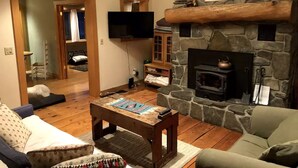 Un salon chaleureux avec une cheminée en pierre, un téléviseur à écran plat fixé au-dessus, et une table basse en bois placée au centre.