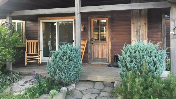 Une cabane en bois avec un porche, une porte-fenêtre coulissante et une porte d’entrée.