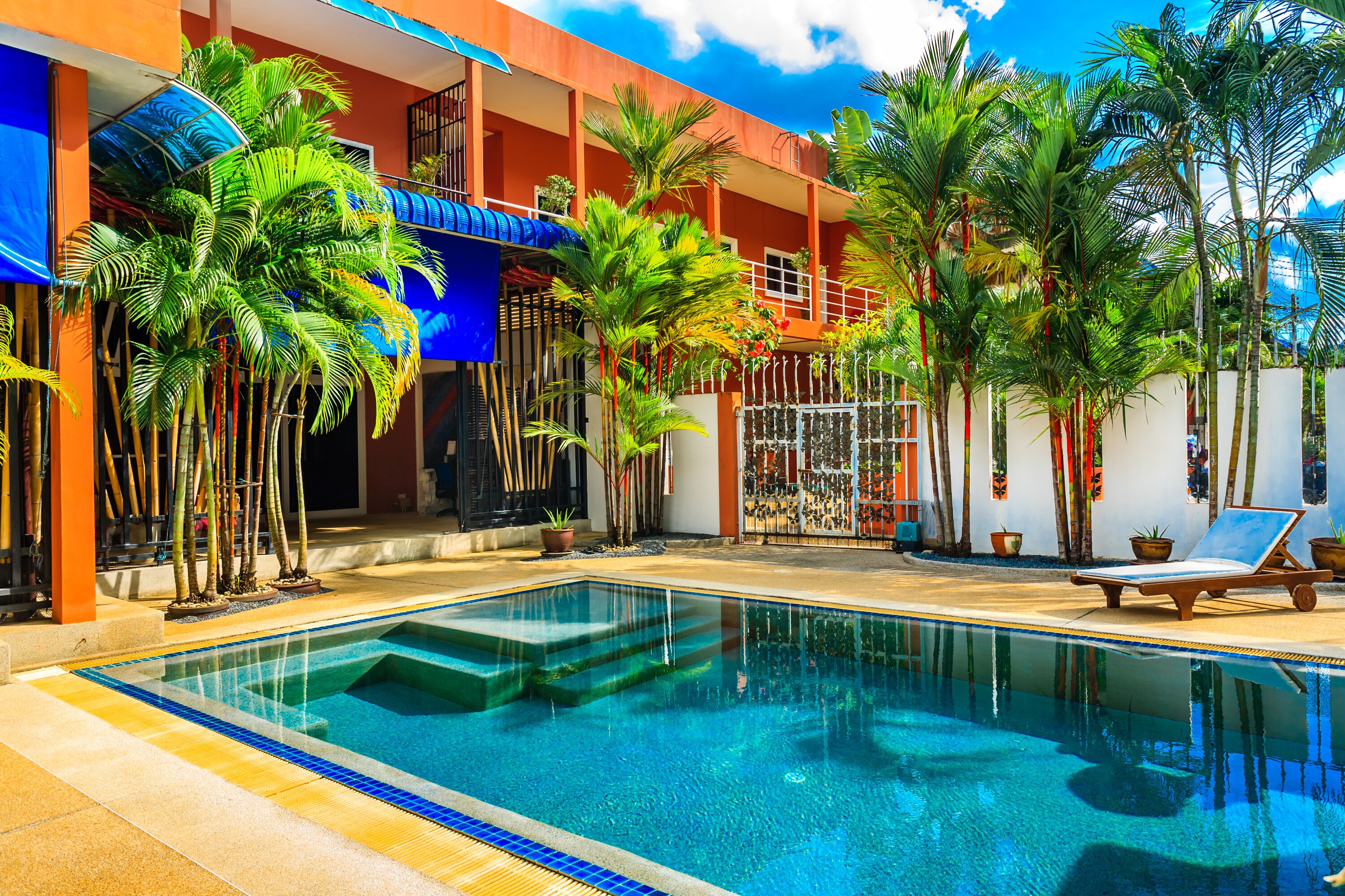 Une piscine bordée de bleu, entourée de palmiers et d’un bâtiment doté de balcons.
