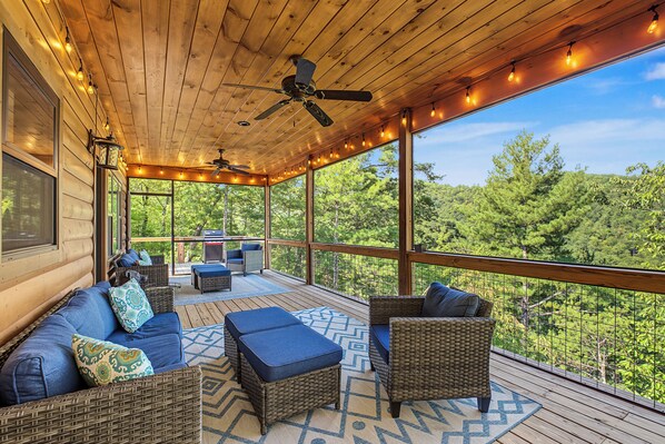 A covered outdoor deck with wicker furniture, a ceiling fan, and string lights.