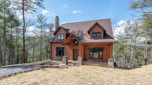 A log cabin with a chimney, a porch, and a view of a forested area.