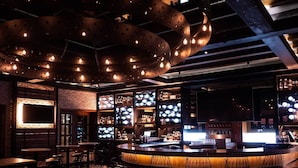 Zona de bar con una barra curva, diversas opciones de asiento y un diseño moderno de techo con vigas y luminarias expuestas.
