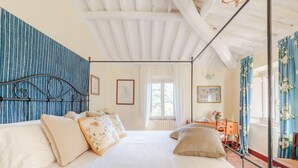 Une chambre à coucher avec un grand lit, une tête de lit en bois, une fenêtre avec des rideaux et un petit bureau avec une chaise.