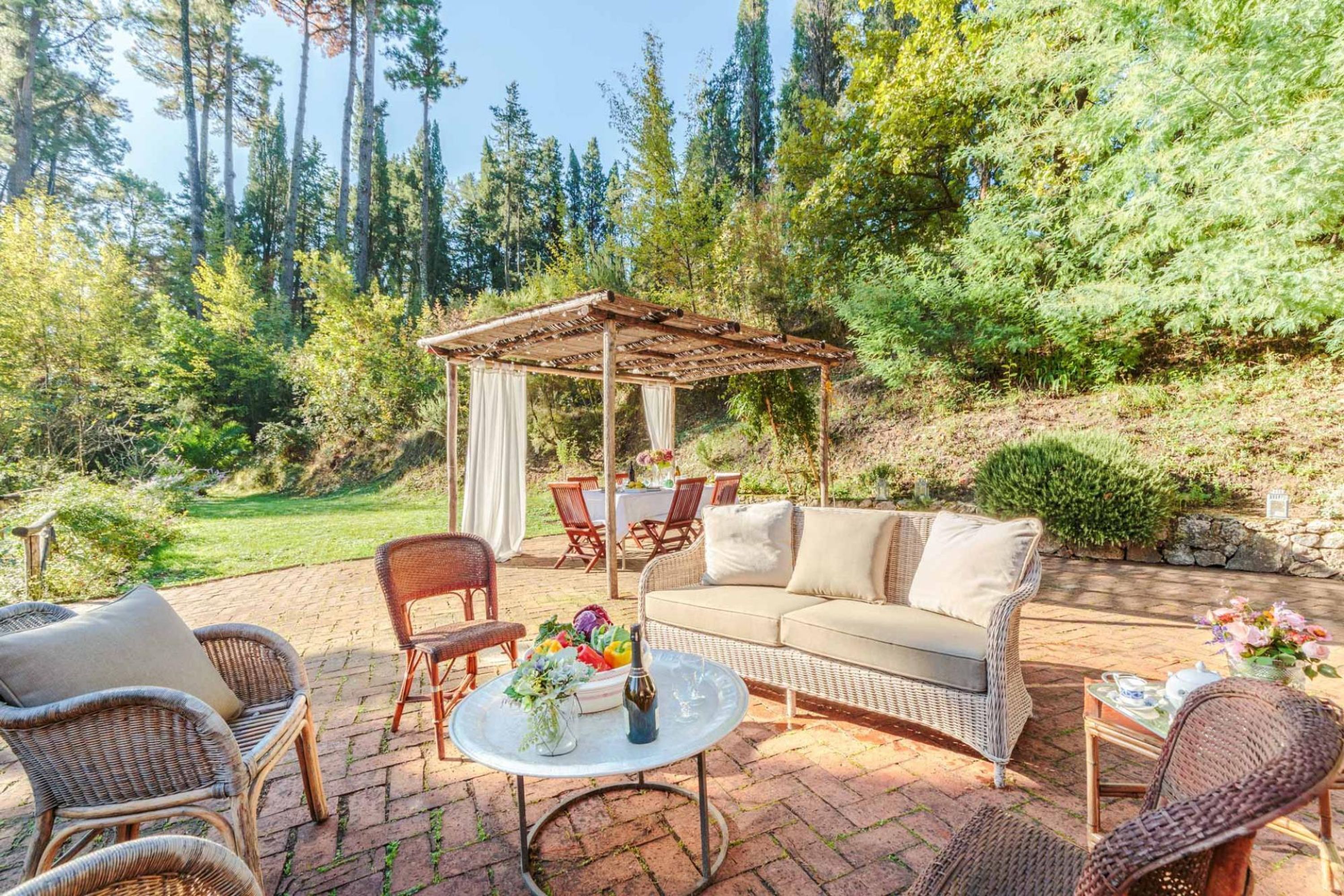 An outdoor patio with wicker furniture, a covered seating area, and a table with a vase of flowers.