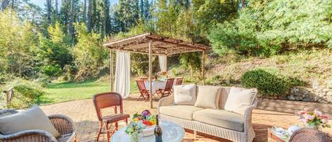 An outdoor patio with wicker furniture, a covered seating area, and a table with a vase of flowers.