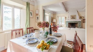 Un coin repas avec une table dressée pour quatre personnes, une cheminée et un salon confortable en arrière-plan.