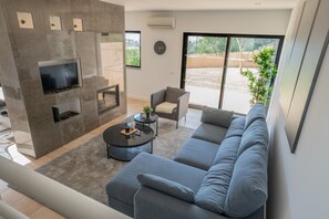 A modern living room with a grey sofa, a flat-screen TV, a fireplace, and a large window offering a view of the outdoors. - #111 Patroves Ocean View by Home Holidays (Albufeira)