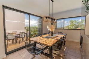 A modern dining area with a wooden table, chairs, and a glass partition. - #111 Patroves Ocean View by Home Holidays (Albufeira)
