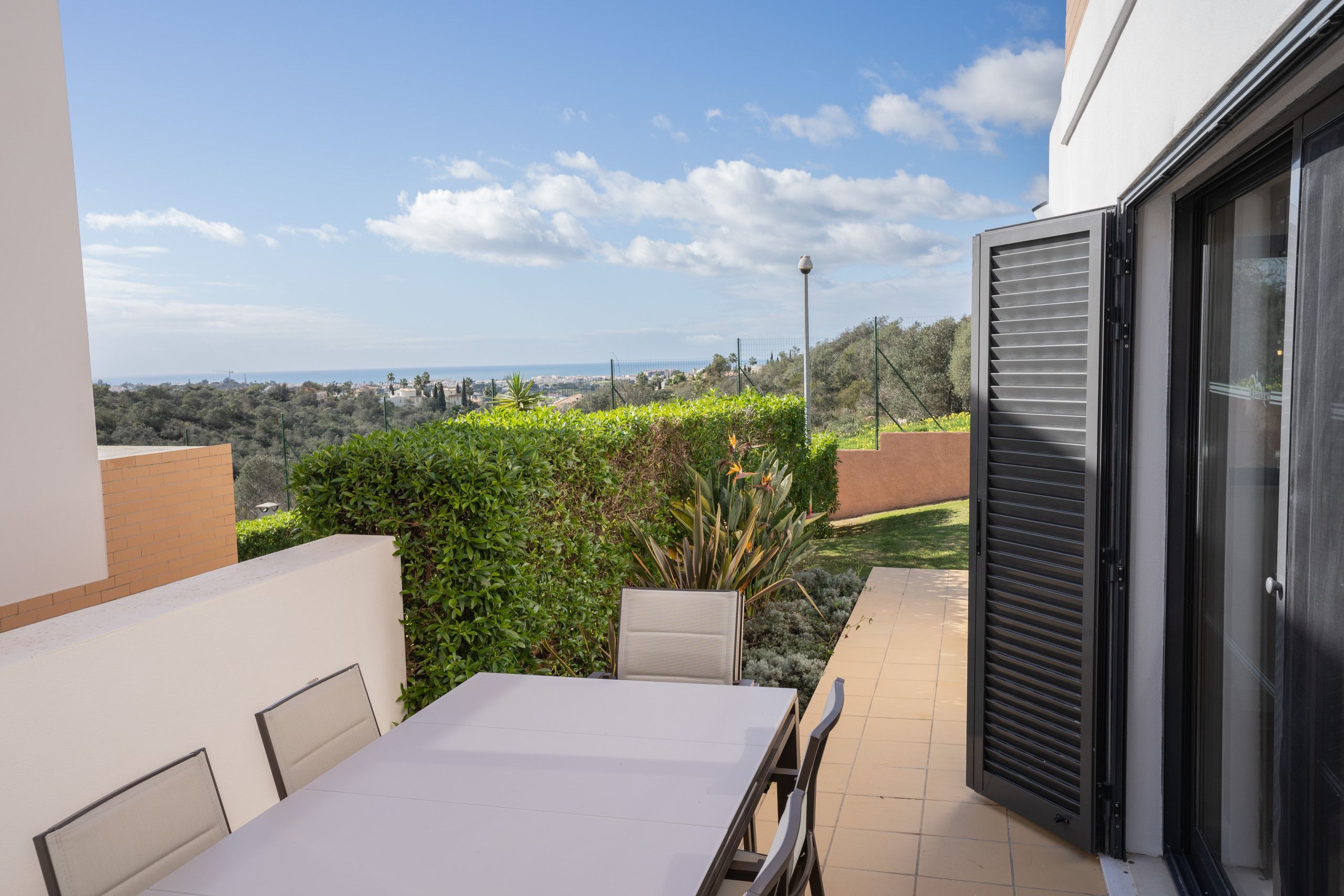 A patio with a table and chairs, a view of the sea, and a building with a sliding door.