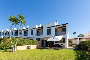 Ein modernes Mehrfamilienhaus mit Balkonen, einer Terrasse mit Gartenmöbeln und einem gepflegten Rasen.