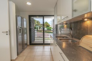 Eine moderne Küche mit einem Edelstahlkühlschrank, einer doppelten Spüle und Blick auf einen angelegten Garten durch eine Glastür.