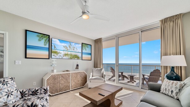 Un salon spacieux doté d’une grande fenêtre donnant sur la plage, d’un ventilateur de plafond et d’une table basse moderne.