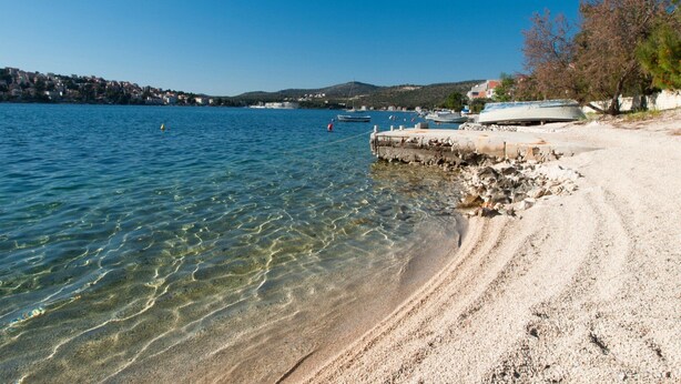 A clear lake with boats, a sandy beach, and a distant town. - Apartments Happy Holiday (Rogoznica)