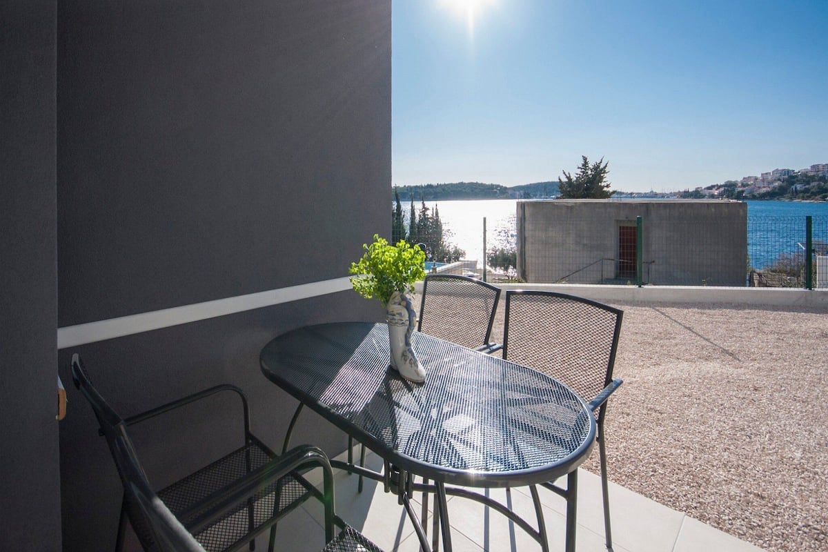 Un balcon avec une table et des chaises, un pot de fleurs et une vue sur une étendue d’eau et des bâtiments éloignés.
