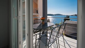 An open balcony with a table and chairs, a vase with flowers, and a view of a body of water and distant hills. - Apartments Happy Holiday (Rogoznica)