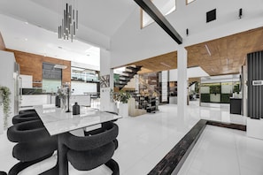 A spacious modern kitchen with a large island, a dining area with a marble table, and a staircase leading to an upper level. - Luxury Villa (Los Angeles)