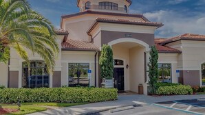 A modern building with a central entrance, a parking area, and a palm tree. - Beautiful Naples Retreat! (Naples)