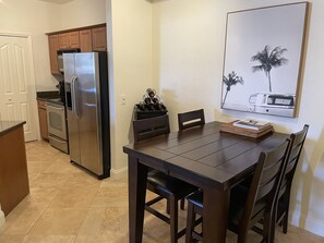 La cuisine est équipée d’un réfrigérateur, d’un four et d’un four à micro-ondes. On y trouve une table à manger avec des chaises, ainsi qu’un tableau encadré accroché au mur.