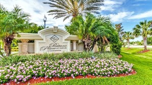 A sign for Postano Place at Naples Condominium surrounded by a well-maintained garden with pink flowers and palm trees. - Beautiful Naples Retreat! (Naples)
