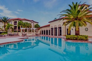 A swimming pool with a clear blue water surface, surrounded by palm trees and a building with a red-tiled roof. - Beautiful Naples Retreat! (Naples)