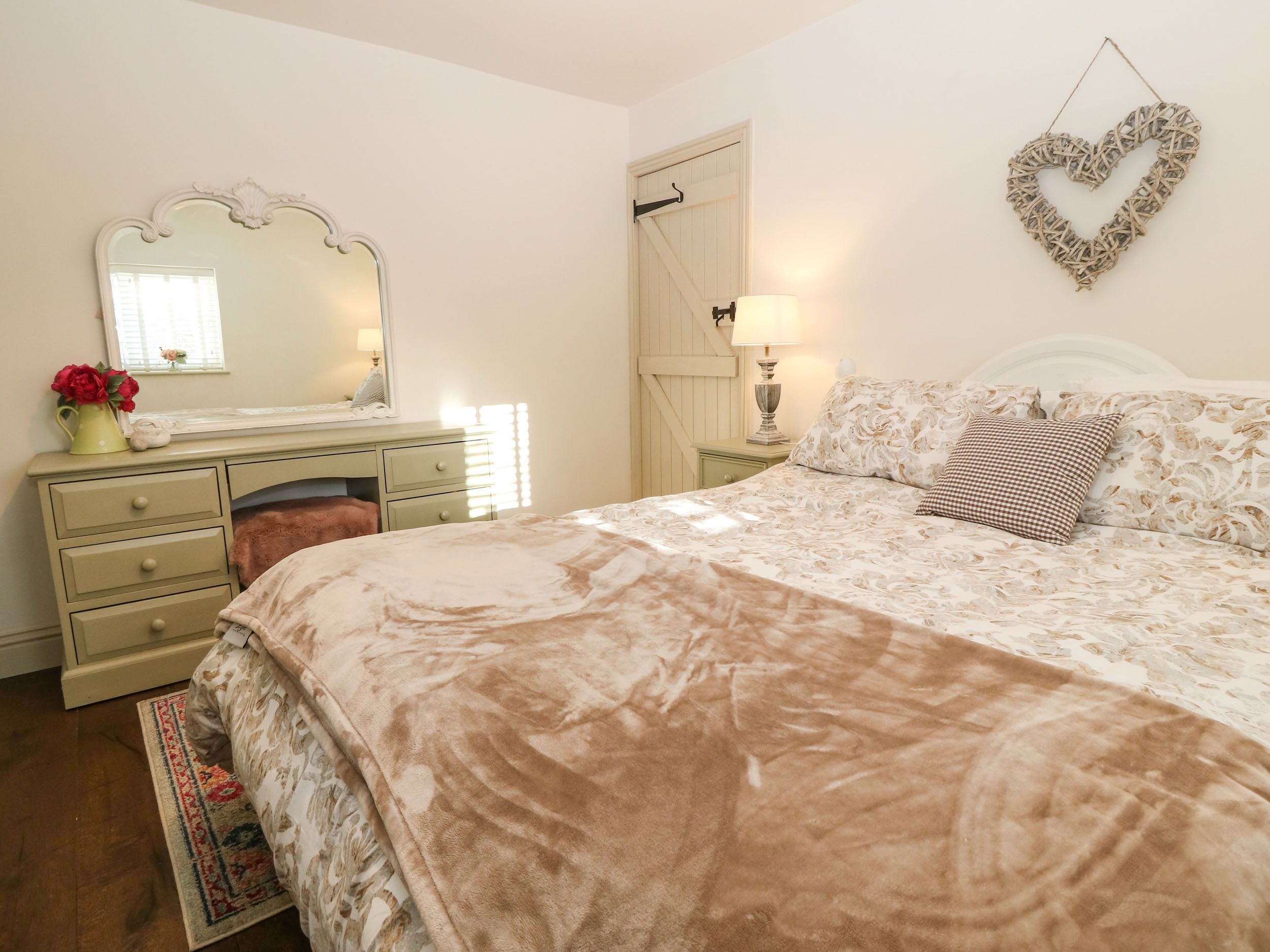 Un dormitorio con cama, cómoda, espejo y una decoración de corazón en la pared.