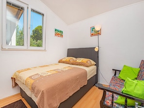 Un dormitorio con una cama, una mesita de noche, una silla, un ventanal y dos lámparas de pared.