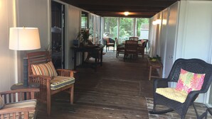 Une véranda au plancher de bois, avec une table et des chaises, un fauteuil à bascule et une lampe.