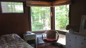 Une chambre avec deux lits, un bureau, une chaise, une commode et une fenêtre donnant sur des arbres.