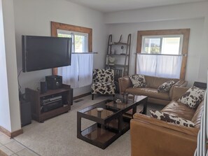 A living room with a flat-screen TV, a sofa with cowhide cushions, a coffee table, and a bookshelf.